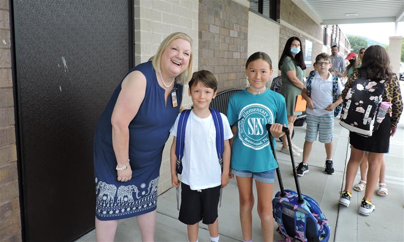 A principal smiles next to two students